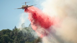 In this Sunday, Aug. 5, 2018, file photo, an air tanker drops fire retardant on a burning hillside in the Ranch Fire in Clearlake Oaks, Calif.