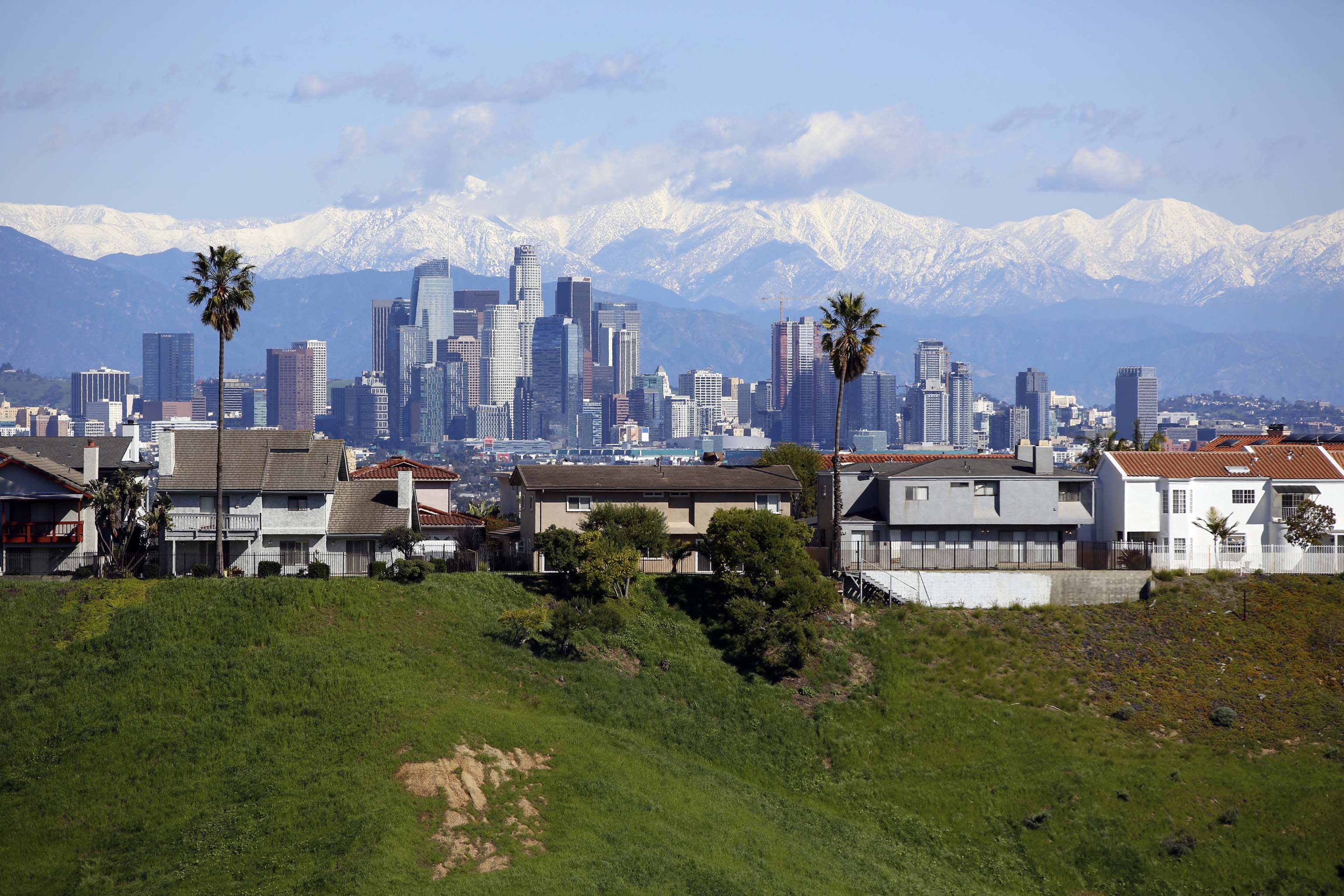 FILE - This Wednesday, Feb. 6, 2019 file photo shows California's mountains glistening with snow behind the Los Angeles skyline and homes above a normally-brown hillside. In just a matter of weeks, a very wet winter has greatly reduced drought conditions in California as a series of storms coated mountains with heavy blankets of snow and unleashed drenching rains. The U.S. Drought Monitor reports Thursday, Feb. 7, 2019 that about a third of the state has no significant dryness and only about 10 percent of the state falls into categories of drought. (AP Photo/Damian Doverganes, File)