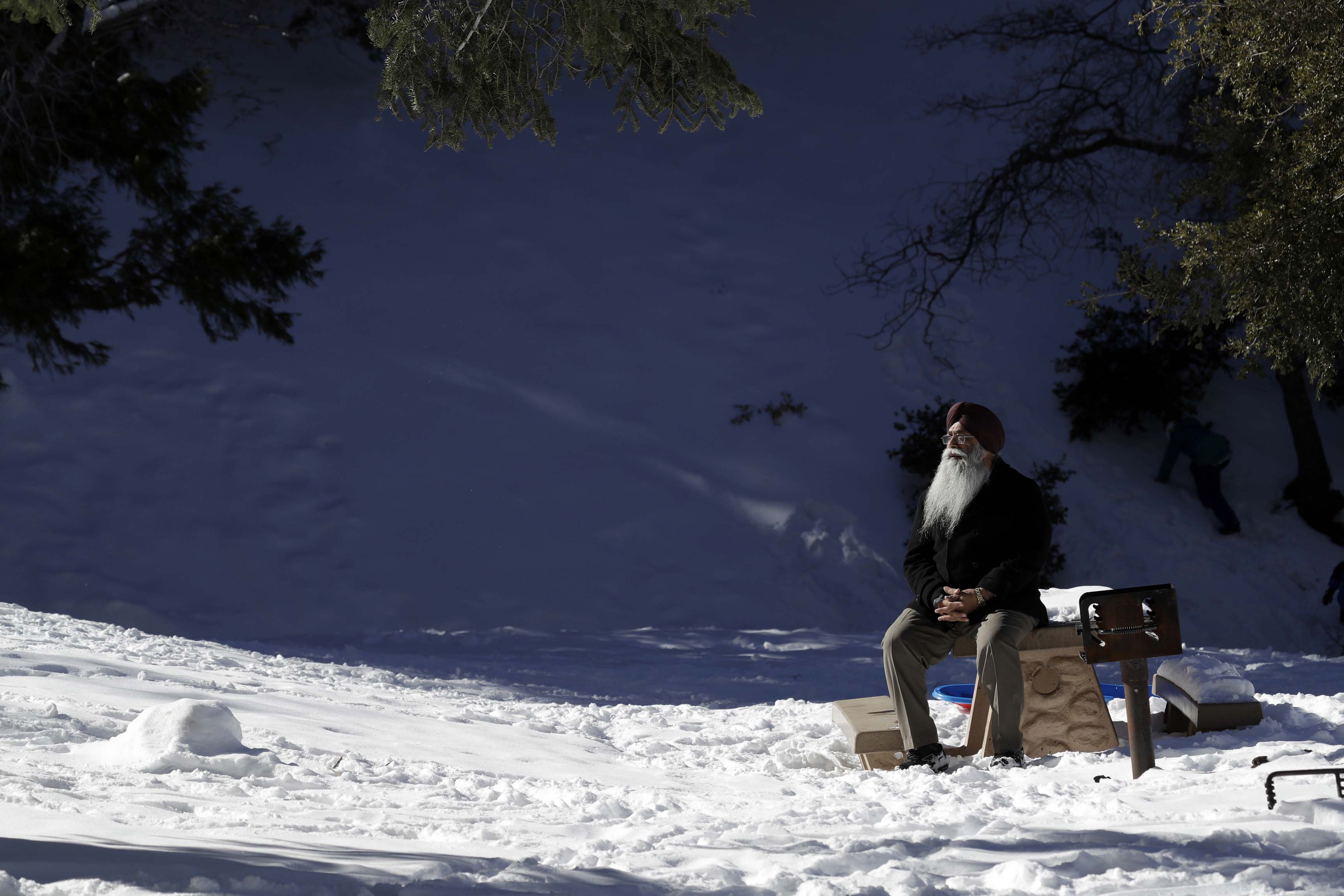 A visitor sits on a park bench under a snow-covered landscape Friday, Feb. 22, 2019, in Wrightwood, Calif. A winter storm swept through the Southwest and brought a rare snowfall to the Las Vegas Strip and the mountains above Malibu in California. (AP Photo/Marcio Jose Sanchez)