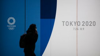 A man with a mask walks past a display promoting the Tokyo 2020 Olympics Monday, Feb. 24, 2020, in Tokyo. (AP Photo/Jae C. Hong)