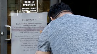 A man takes a photo of a sign advising that the Employment Development Department is closed due to coronavirus concerns, in San Francisco on Thursday, March 26, 2020.