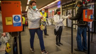 An employee working for the regional public transport company offers a face mask to a passenger at the Nyugati square in Budapest, Hungary, Monday, April 27, 2020.