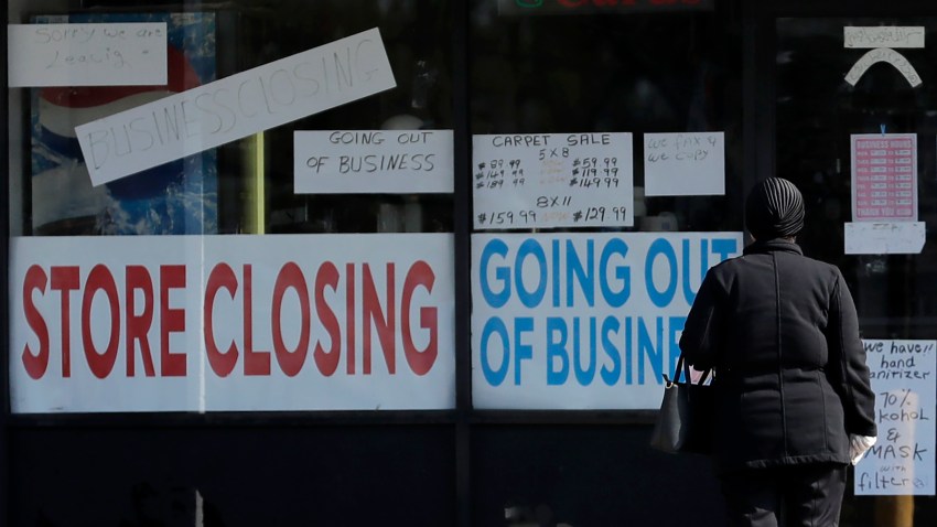 In this May 13, 2020, file photo, a woman looks at signs at a store closed due to COVID-19 in Niles, Ill.,