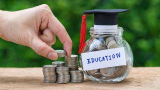 Woman hand holding stack of coins money and glass jar with full of coins and graduates hat label as Education, education or savings concept.