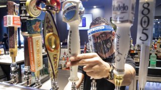 In this July 1, 2020, file photo, a bartender pours a beer while wearing a mask and face shield amid the coronavirus pandemic at Slater's 50/50 in Santa Clarita, Calif.