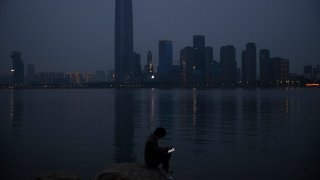 In this April 5, 2020, file photo, a man checks his mobile phone along the Yangtze River in Wuhan in central China's Hubei province. As governments around the world consider how to monitor new coronavirus outbreaks while reopening their societies, many are starting to bet on smartphone apps to help stanch the pandemic.