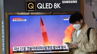 A man walks past a screen showing file footage of a North Korean missile test
