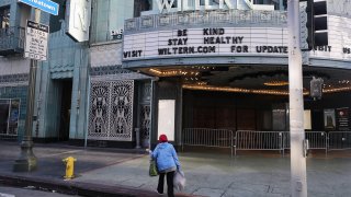 A person walks outside the shuttered Wiltern Theater, with the message ‘Be Kind Stay Healthy’ written on the marquee, as the coronavirus pandemic continues on March 23, 2020 in Los Angeles, California. (Photo by Mario Tama/Getty Images)