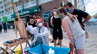 A local artist and onlookers wear masks on the boardwalk during the Memorial Day holiday weekend on May 23, 2020 in Ocean City Maryland. - The beach front destination has lifted its COVID-19 related beach and boardwalk restrictions May 9 and lodging restrictions May 14. The state of Maryland moved from a stay-at-home order to safe-at-home order May 15. (Photo by Alex Edelman / AFP) (Photo by ALEX EDELMAN/AFP via Getty Images)