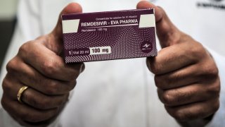 Gloved hands hold a box of coronavirus drug Remdesivir.