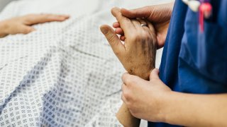 Close-up shot of hand's of a female doctor measuring pulse of a lying senior patient