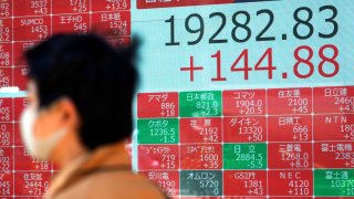 In this April 23, 2020, file photo, a man wearing a mask walks past an electronic stock board showing Japan's Nikkei 225 index at a securities firm in Tokyo.