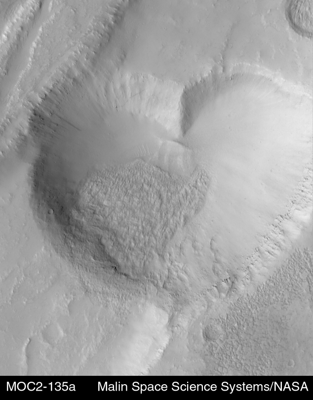 "The heart-shaped pit is about 2.3 kilometers (1.4 miles) at its widest. The image was targeted by the MOC team in order to examine the relationship between a lava flow (margins indicated by white arrows, above right) and the graben and pits that disrupted and cut across the flow. The graben, pit, and lava flow are located on the east flank of the Alba Patera volcano in northern Tharsis." Released in 1999.