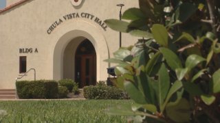A tan Chula Vista City Hall stands behind a green bush
