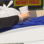 A hand places a cup and bag on the hood of a car, covered with a blue towel