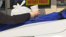 A hand places a cup and bag on the hood of a car, covered with a blue towel