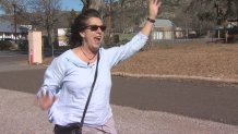 Woman with dark hair and a light colored shirt stands waving her arms in the wind