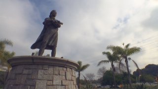 Tall statue stands on a stone pedestal with a cloudy sky in the background