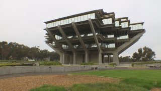 An oddly shaped building stands on a green hill with a cloudy sky.