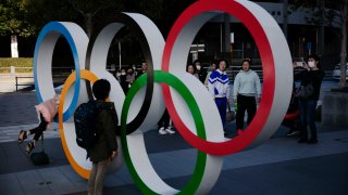 In this Feb. 23, 2020, file photo, people wait in line to take pictures with the Olympic rings near the New National Stadium in Tokyo, Japan.