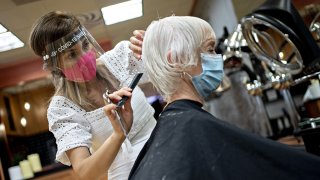 In this May 29, 2020, file photo, a stylist wearing a protective face shield and mask cuts a customers hair at a salon in Arlington, Virginia.