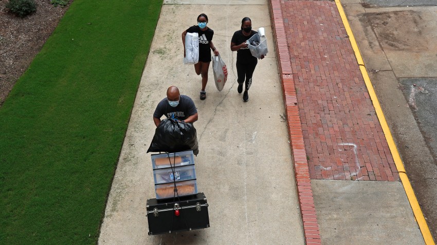 A family carries their belongings while college students begin moving in for the fall semester