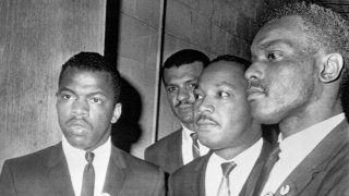 Reverend Martin Luther King Jr., (center) is escorted into a mass meeting at Fish University in Nashville. His colleagues are, left to right, John Lewis, national chairman of the Student Non-Violent Committee and Lester McKinnie, on of the leaders in the racial demonstrations in Nashville recently. King gave the main address to a packed crowd.