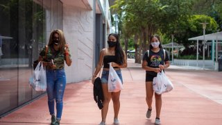 Shoppers carrying bags wear protective masks in Miami Beach, Florida, U.S., on Friday, July 17, 2020.
