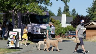 Bobby Price, right, and Catherine Vogt, center, walk with Catherine's daughter Avery, 8, and their dogs after ordering food and drinks from the YS Street Food and Dreamy Drinks food trucks, Monday, Aug. 10, 2020, near the suburb of Lynnwood, Wash.