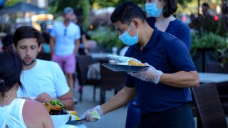 A waiter wearing a protective mask serves food to patrons