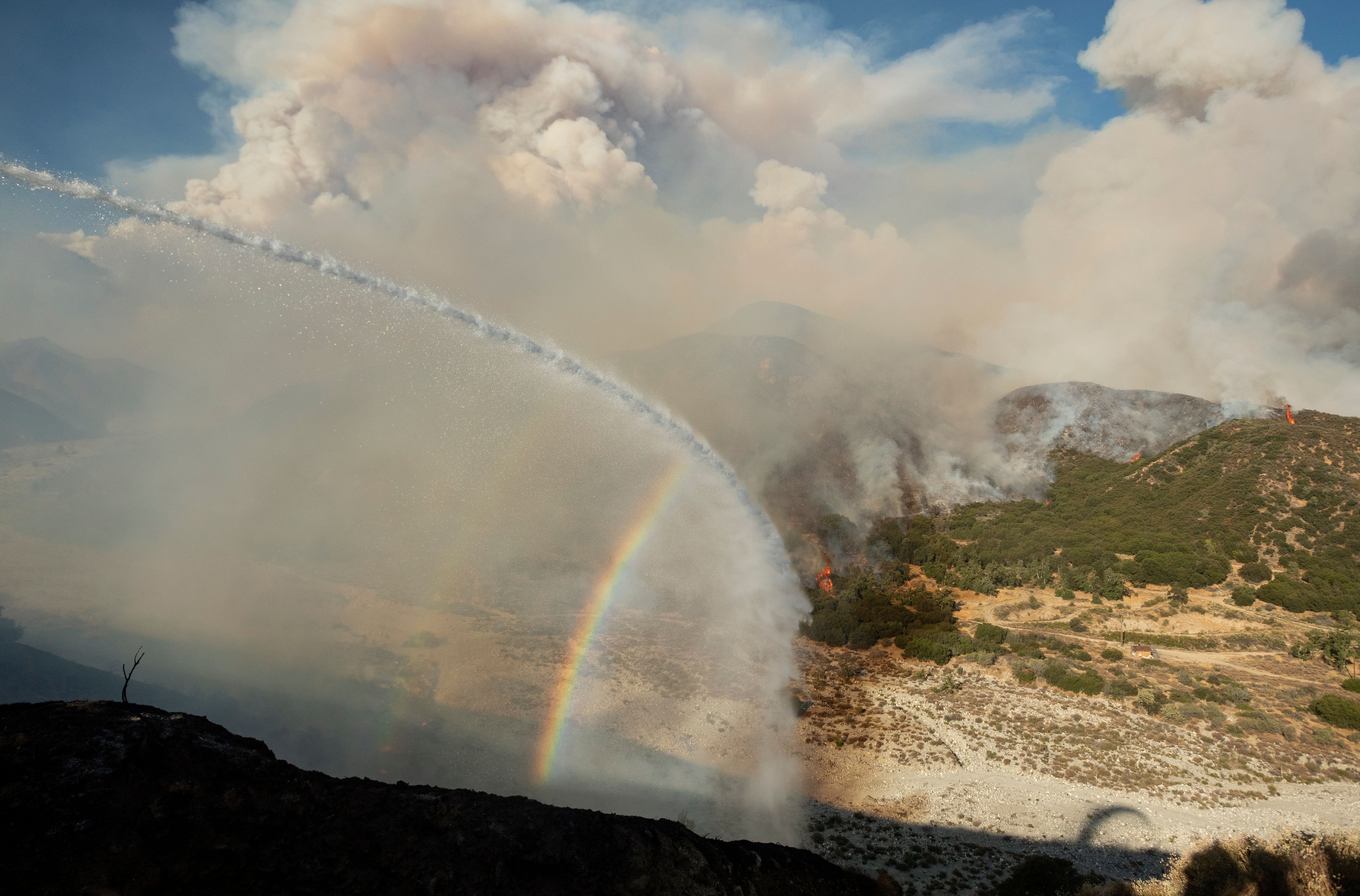 Water from a fire engine creates a rainbow near flames as firefighters continue to battle the Apple fire near Banning, California on August 1, 2020. – 4,125 acres have burn in Cherry Valley, about 2,000 people have received evacuation orders in the afternoon of August 1.<br />nAround 8PM the fire spread to 12,000 acres. (Photo by JOSH EDELSON / AFP) (Photo by JOSH EDELSON/AFP via Getty Images)