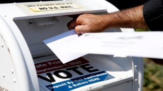 In this Aug. 23, 2020, file photo, a voter drops a ballot into the box for mail-in ballots outside of Newton City Hall in Newton, MA, where there's a crowded field in the primary race for the fourth Congressional Democratic nomination.