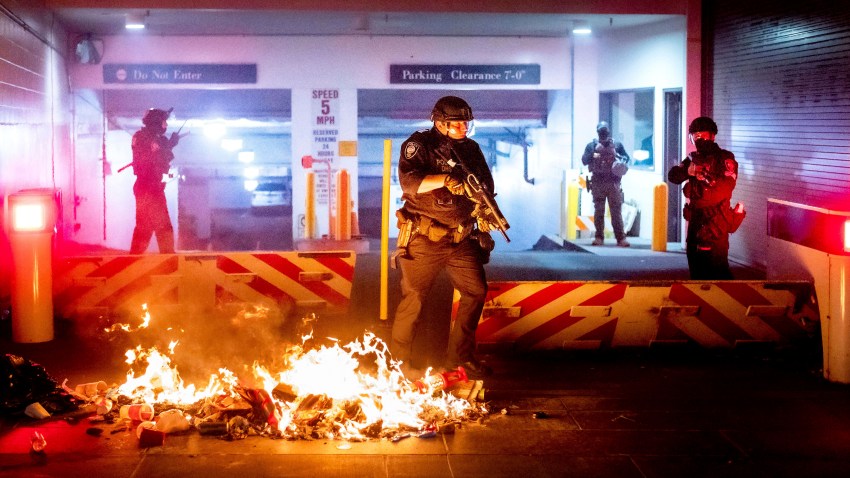A Department of Homeland Security officer emerges from the Mark O. Hatfield United States Courthouse after demonstrators lit a fire on Sunday, Aug. 2, 2020, in Portland, Ore. Following an agreement between Democratic Gov. Kate Brown and the Trump administration to reduce federal officers in the city, nightly protests remained largely peaceful without major confrontations between protesters and officers.