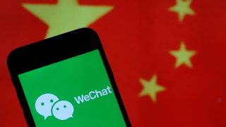 The WeChat logo is displayed on the screen of a smartphone in front of a Chinese flag