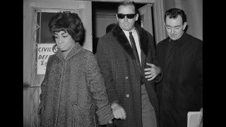 Jack "Murf the Surf" Murphy, wearing dark glasses, is taken from a police station where he was held overnight on a hotel robbery charge, to court for arraignment. Murphy was arrested January 4th as he emerged from a hearing held in connection with charges that he and two others stole $400,000 in gems from New York City's Museum of Natural History. The man at right is an unidentified detective.