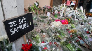 A poster reading "I am Samuel" and flowers lay outside the school where slain history teacher Samuel Paty was working, Saturday, Oct. 17, 2020 in Conflans-Sainte-Honorine, northwest of Paris