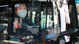 A San Diego MTS bus driver wears a mask behind a barrier from her seat.