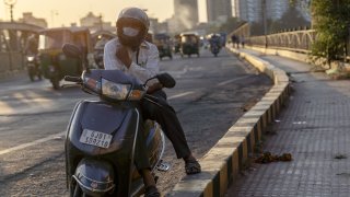 A motorcyclist wears a protective mask while sitting at the side of the road at the Sabarmati Riverfront in Ahmedabad, India, on Thursday, Oct. 22, 2020. Prime Minister Narendra Modi said his government will ensure that all 1.3 billion people nationwide will have access to a Covid-19 vaccine as soon it is ready.