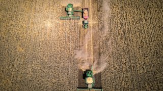 A farmer operates a combine harvester as he unloads wheat into a grain cart during a harvest at a farm near Gunnedah, New South Wales, Australia, on Tuesday, Nov. 10, 2020.