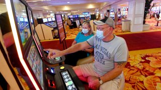 Char Hentschel (L) of Illinois looks on as Bill Hentschel of Illinois plays a slot machine at the Tropicana Las Vegas after the Las Vegas Strip resort reopened for the first time since mid-March because of the coronavirus (COVID-19) pandemic on September 17, 2020 in Las Vegas, Nevada. Penn National Gaming, which manages the property under a lease agreement, originally planned to reopen the property on September 1 but pushed back those plans after reviewing the impact the pandemic had on demand for travel and room nights in Las Vegas.