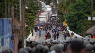Honduran migrants, top, stand next to cargo trucks as they confront Guatemalan soldiers and police