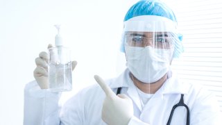 Portrait of a Doctor wearing PPE and pointing a hand sanitizer to disinfect your hands at times of COVID-19 â healthcare and medicine concepts