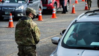 Servicemen coordinate with people in their cars as they line up and wait to be vaccinated