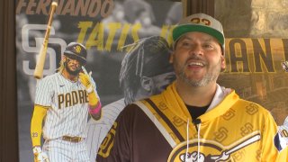Man in a yellow hoodie and ballcap stands in front of a picture of Fernando Tatis, Jr.