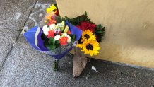 Flowers lean against the wall to the building where a man jumped and landed on top of a woman who was walking on the sidewalk below.