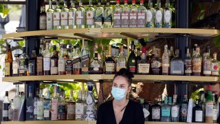 A bartender wears a mask while working at an outdoor bar amid the COVID-19 pandemic Thursday, May 20, 2021, at The Grove in Los Angeles. California regulators will shoot for a mid-June easing of workplace masking and social distancing requirements to conform with a broader state order. They asked to delay a debate Thursday on how quickly they should drop coronavirus safety rules for employees.