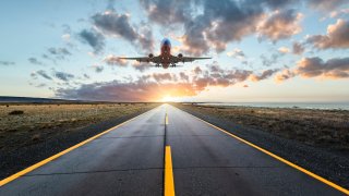 Landing airplane over a highway road at sunset