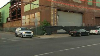 A police SUV and a sedan are parked in front of a warehouse. Philadelphia police said the sedan fell on top of a man and crushed him to death.