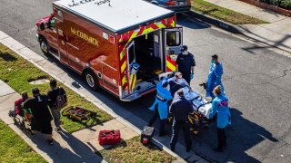 After administering him with oxygen, County of Los Angeles paramedics load a potential Covid-19 patient in the ambulance before transporting him to a hospital in Hawthorne, California on December 29, 2020 as a family walks by.