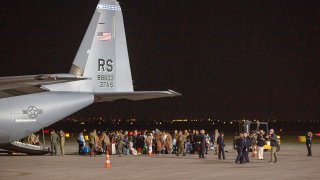 families evacuated from Kabul, Afghanistan, walk past a U.S Air Force plane that they arrived on at Kosovo's capital Pristina International Airport